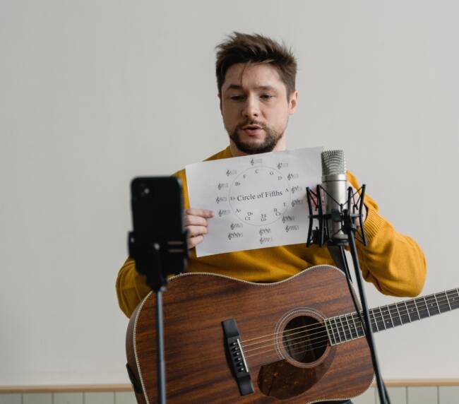 Guitarist reviewing chord structure beside a studio microphone